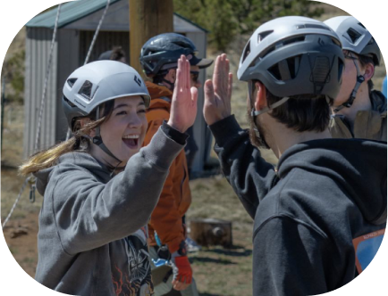 Two DU students in helmets giving each other high-fives outdoors.